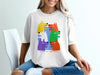 White t-shirt with a playful graphic of six colorful dog heads, "DO NOT LET THEM DRIVE" text.