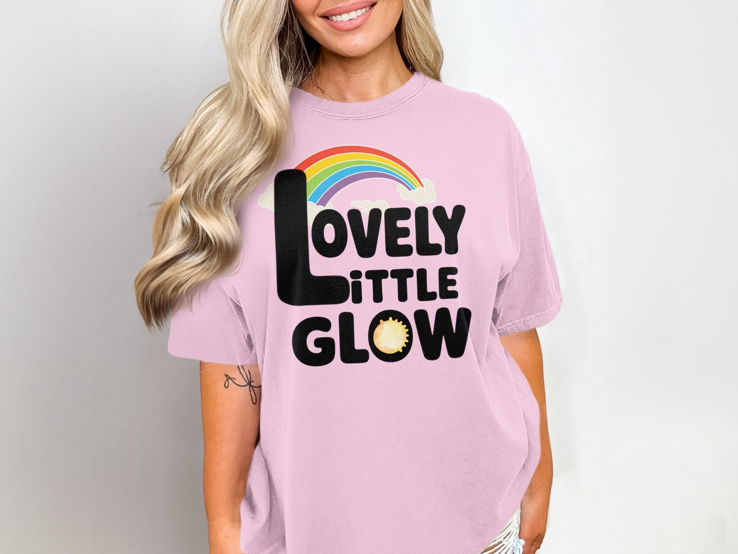 Pink t-shirt with "LOVELY LITTLE GLOW" text, rainbow, and sun graphic.