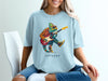 Chameleon wearing sunglasses plays electric guitar on light blue t-shirt.