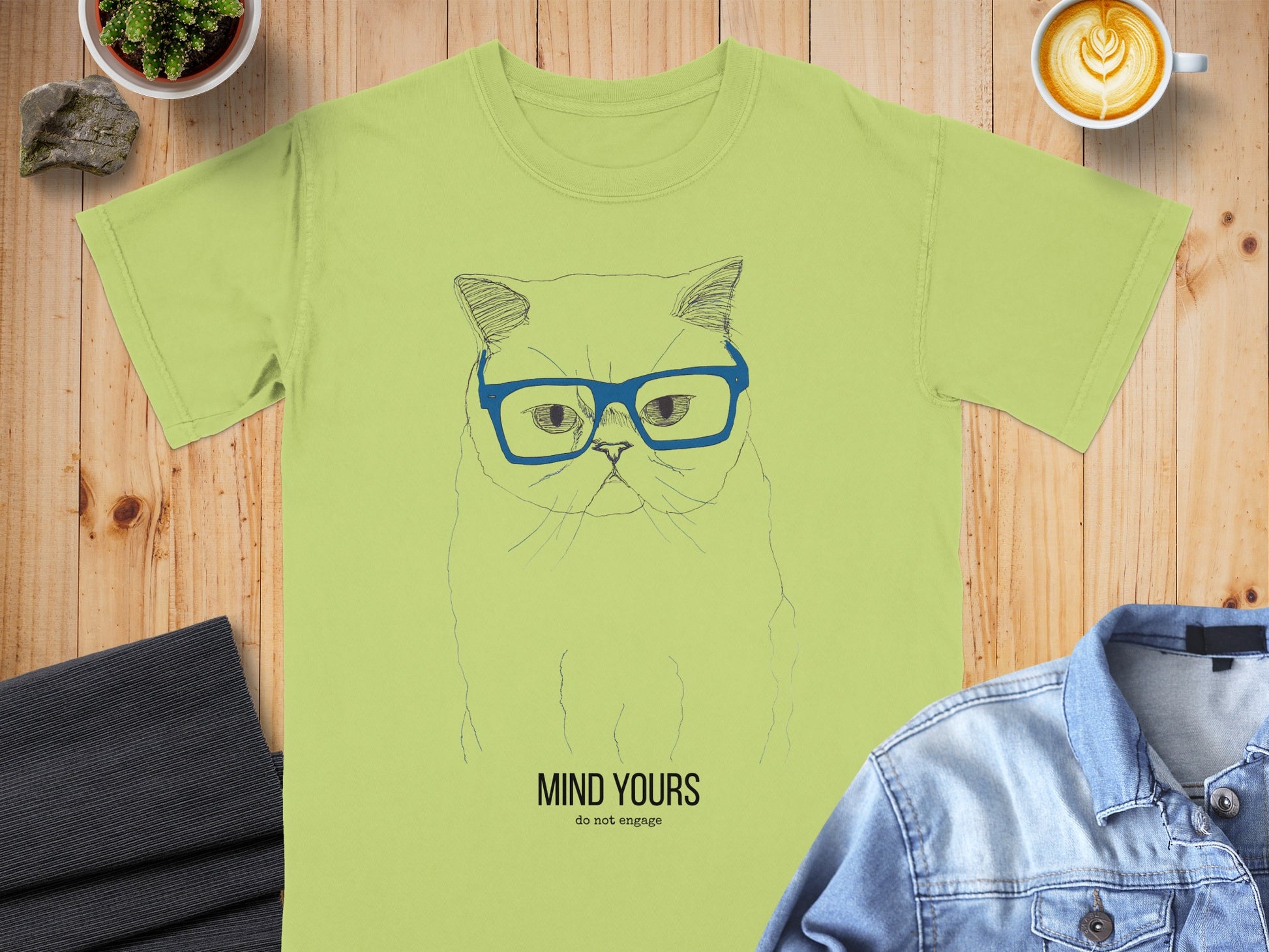 Light green t-shirt with a hand-drawn cat wearing glasses and the text "MIND YOURS do not engage".