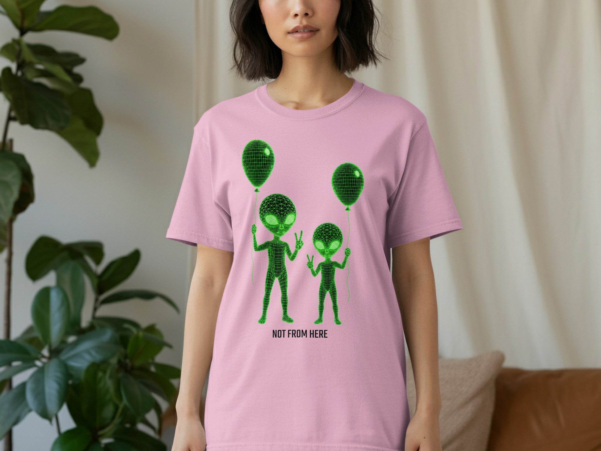 Pink t-shirt with two green aliens holding balloons and the text "NOT FROM HERE".