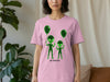 Pink t-shirt with two green aliens holding balloons and the text "NOT FROM HERE".