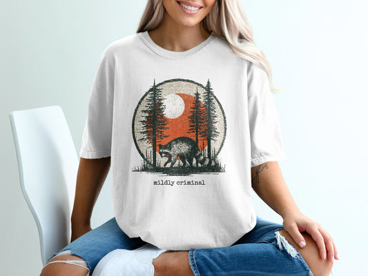 White t-shirt with a vintage graphic of a raccoon in a forest at sunset.