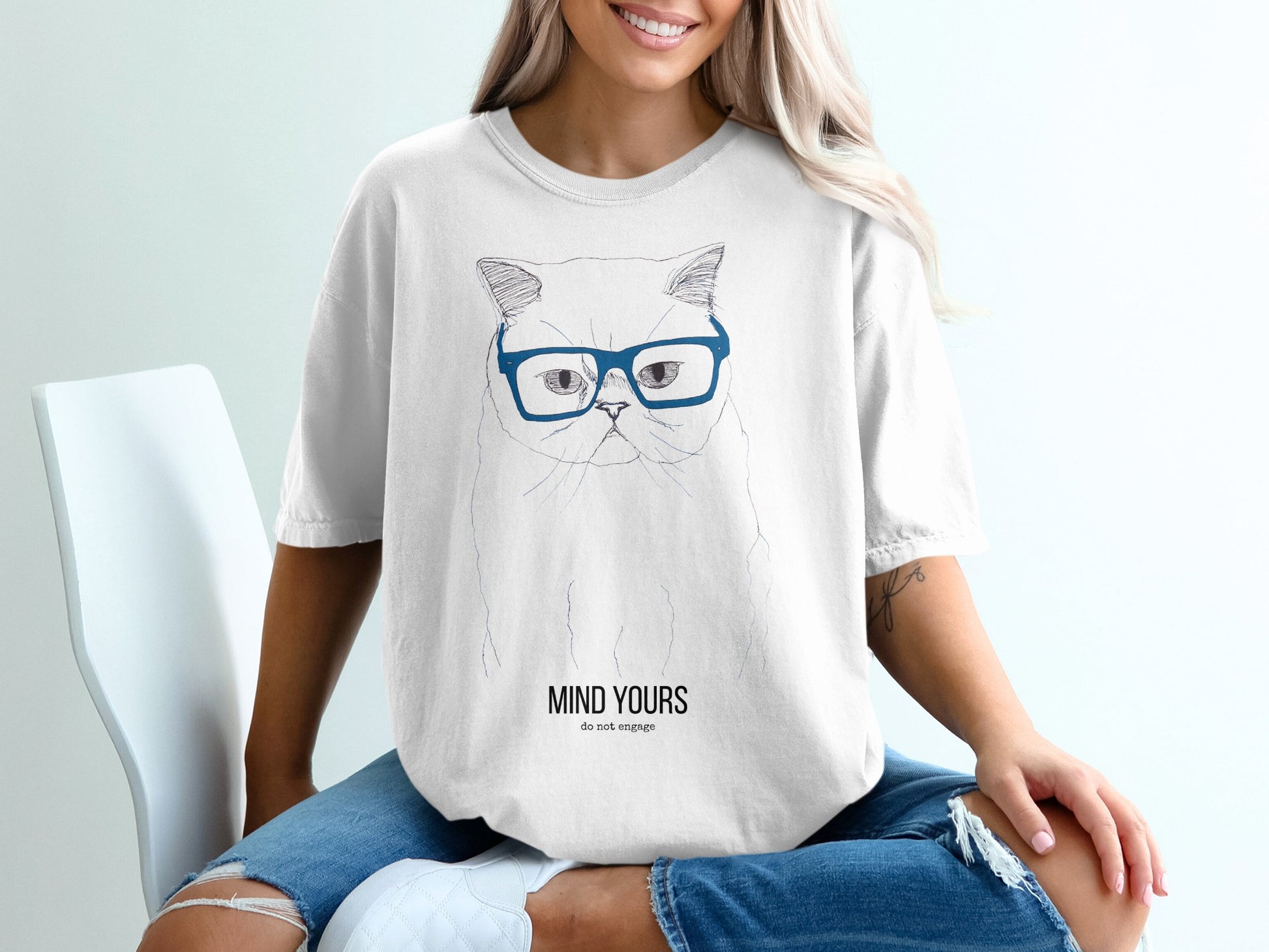 Woman wearing a white t-shirt with a blue-eyed cat graphic and text.