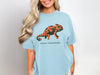 Light blue t-shirt with a black and orange chameleon graphic and "Social Camouflage" text.