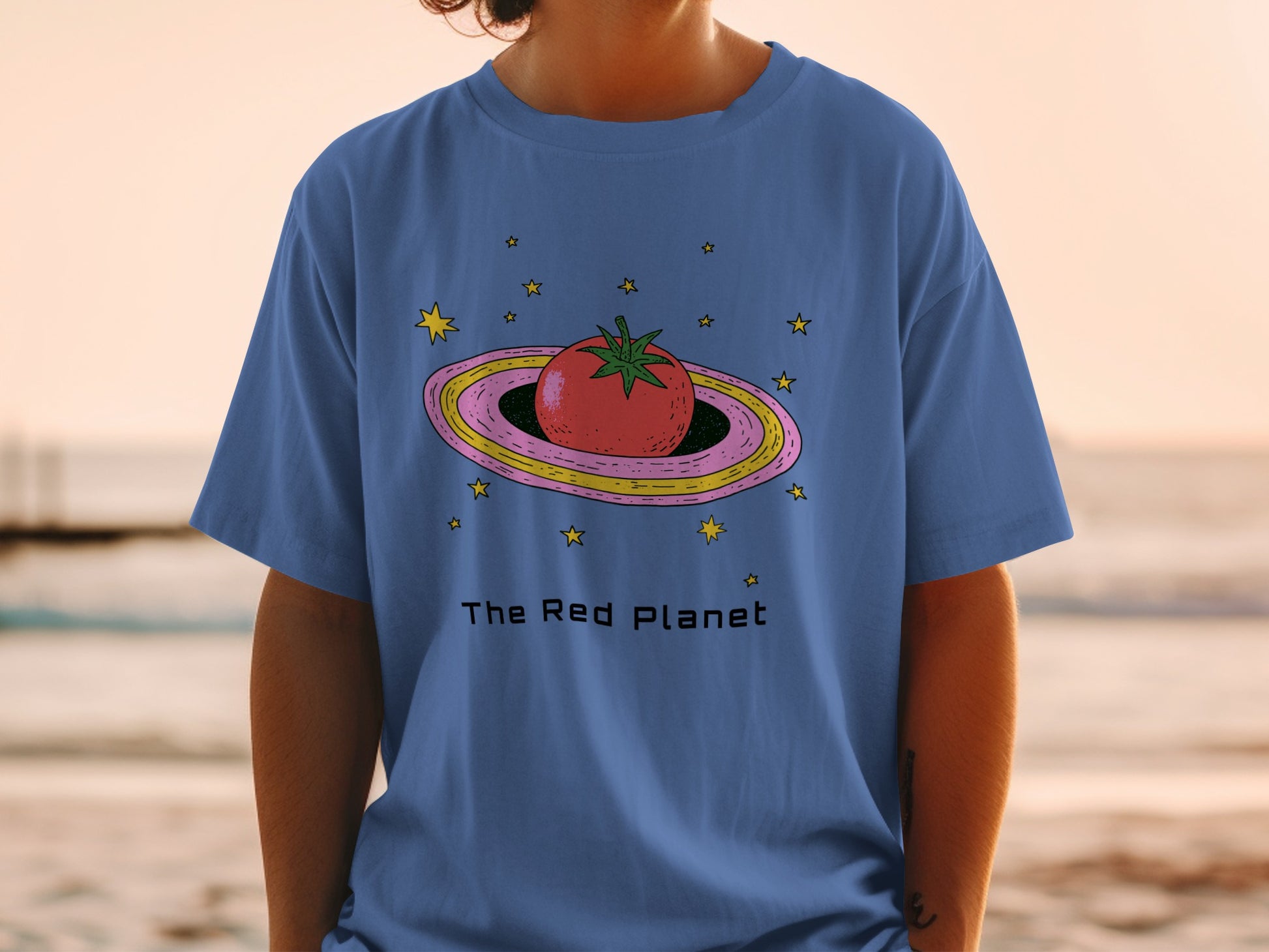 Blue t-shirt with a tomato on a planet and stars graphic.