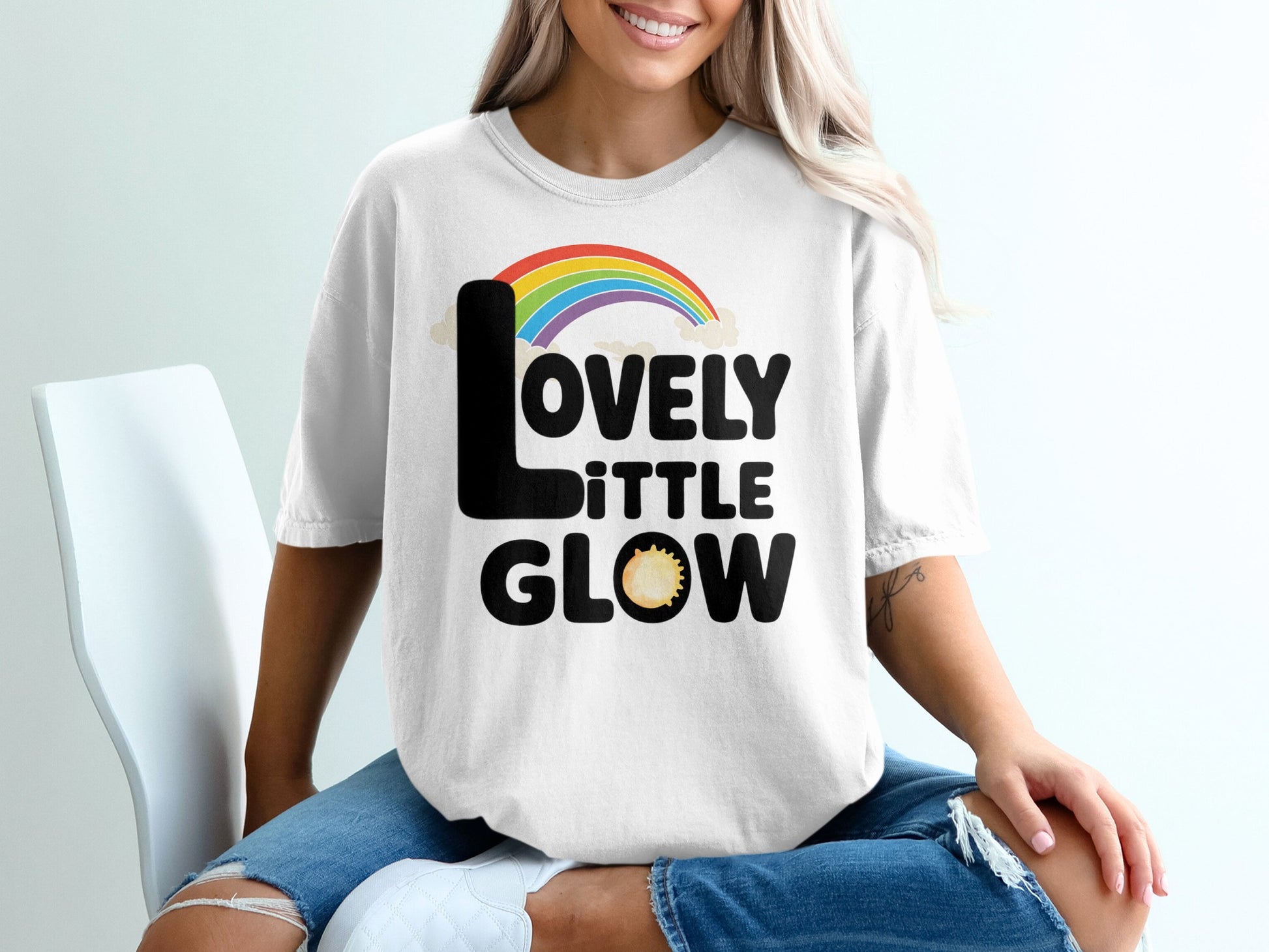 White t-shirt with "Lovely Little Glow" text and rainbow graphic.